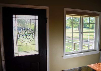 Stained glass door beside window overlooking green yard