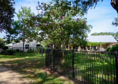 Scenic view of ranch home with lush garden and fence