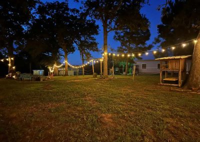 Backyard at dusk with string lights, trees, and playset