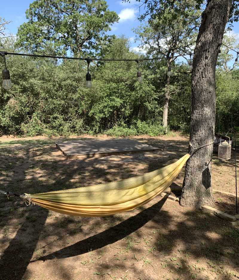 Yellow hammock strung between trees under string lights