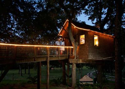 Treehouse illuminated at dusk with couple on balcony